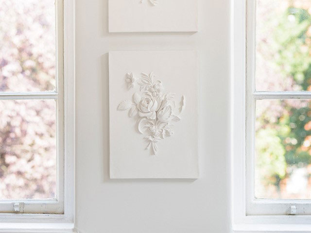 Photo of white plaster 3D artwork by Geoffrey Preston of a posy of flowers, displayed on wall in Helen Amy Murray studio