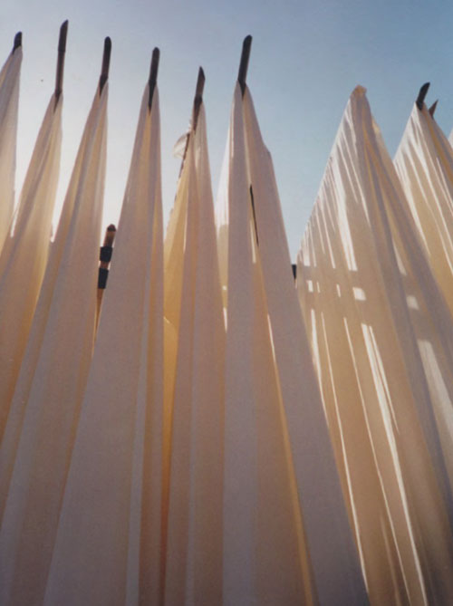Photograph by Helen Murray of fabric drying on poles in India against a blue sky