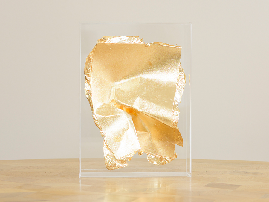 Photograph of a gold leaf paper sculpture by Fredrikson Stallard in a Perspex box on a wooden table with grey background