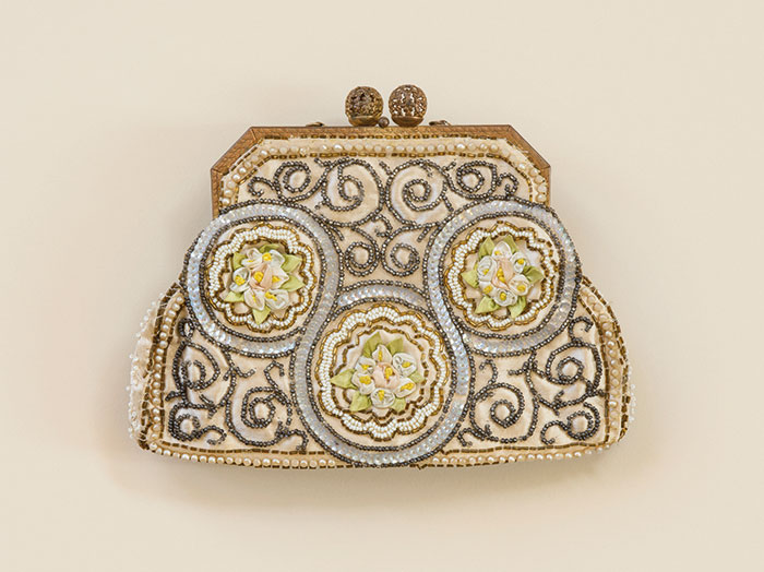 Photograph of a vintage purse with bead work and floral motif embroidery detailing on a cream background