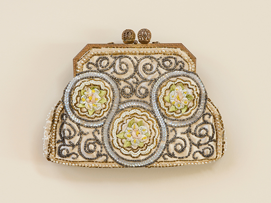 Photograph of a vintage purse with bead work and floral motif embroidery detailing on a cream background