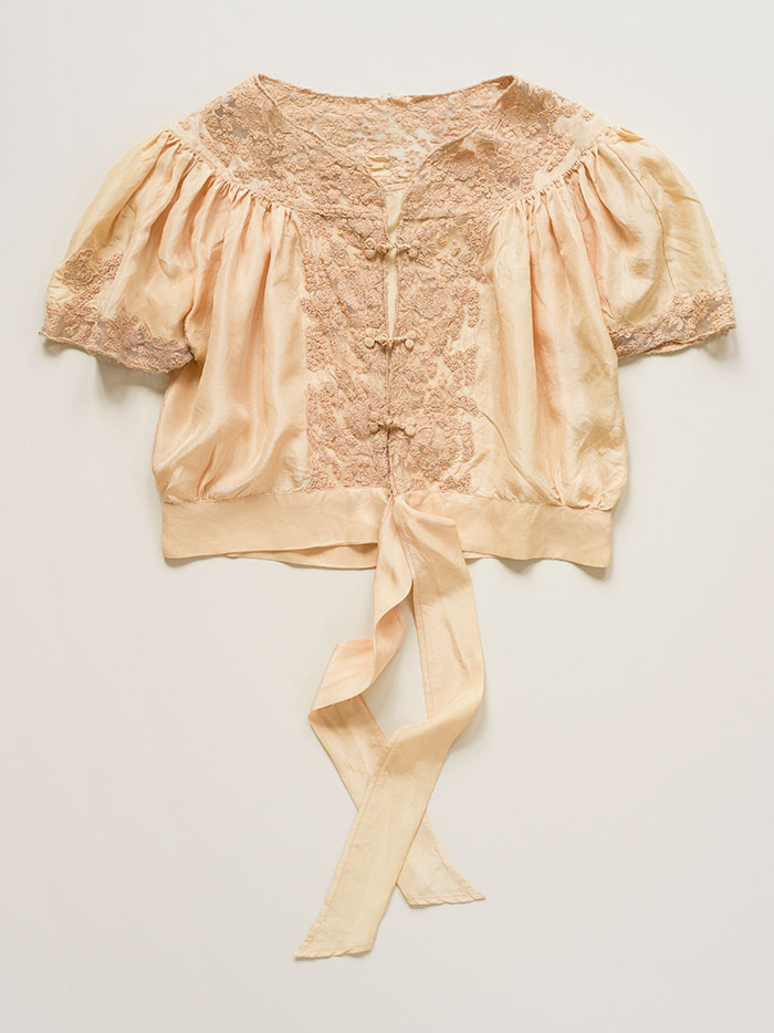 Photograph of an antique peach silk blouse, with delicate embroidered lace detail on white background