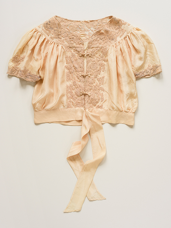 Photograph of an antique peach silk blouse, with delicate embroidered lace detail on white background